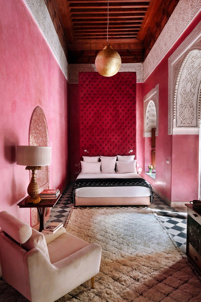 Pink and terracotta Moroccan riad courtyard with luxurious plunge pool, ornate archways, tropical plants and rooftop loungers at sunset