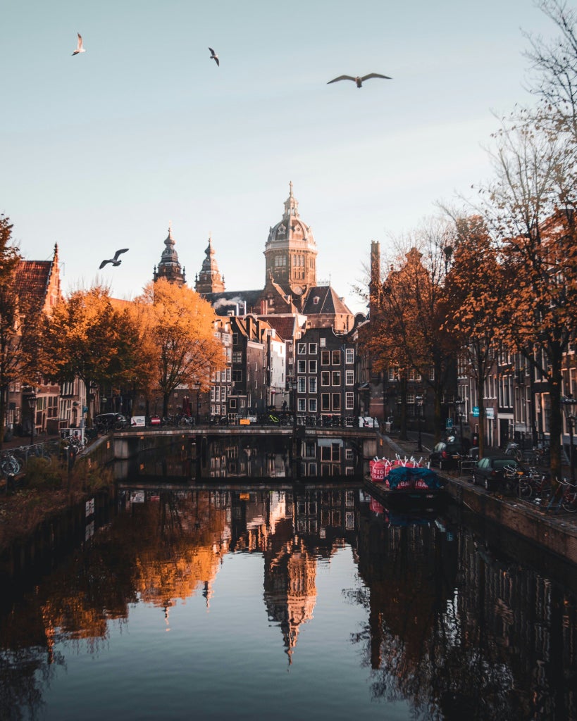 Long wooden canal boat gliding past elegant 17th-century merchant houses along Amsterdam's iconic waterways at golden hour