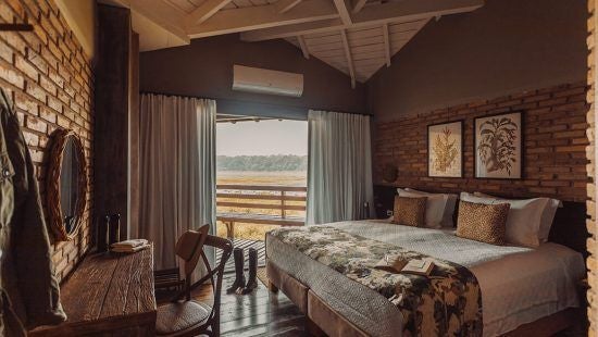 Luxurious private villa at Caiman Ecological Refuge, featuring rustic wooden decor, plush bedding, and panoramic Brazilian wetland views through large windows