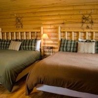 Rustic luxury cabin interior at Zion Mountain Ranch with warm wood paneling, plush bedding, and expansive windows overlooking scenic mountain landscape