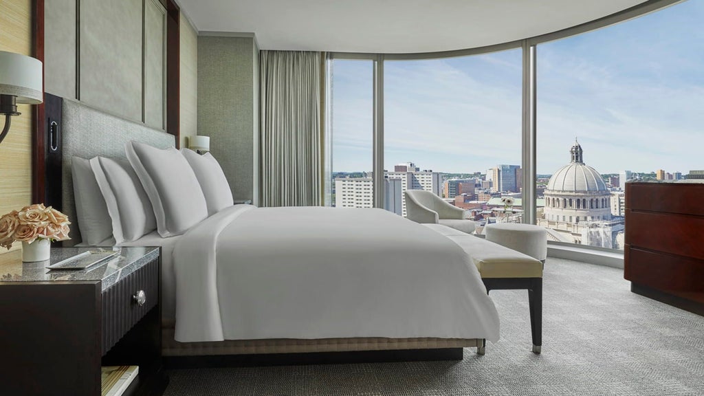 Spacious Four Seasons corner suite with panoramic city views, elegant modern furnishings, plush king bed, and floor-to-ceiling windows overlooking scenset skyline