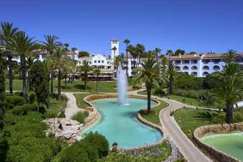 Luxury oceanfront resort in Portugal with white Mediterranean architecture, infinity pools cascading towards Atlantic cliffs and manicured gardens