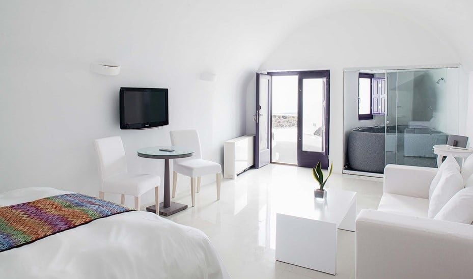 Luxurious white-walled Superior Suite at Katikies Chromata, overlooking Santorini's azure caldera with minimalist design and private balcony with panoramic views