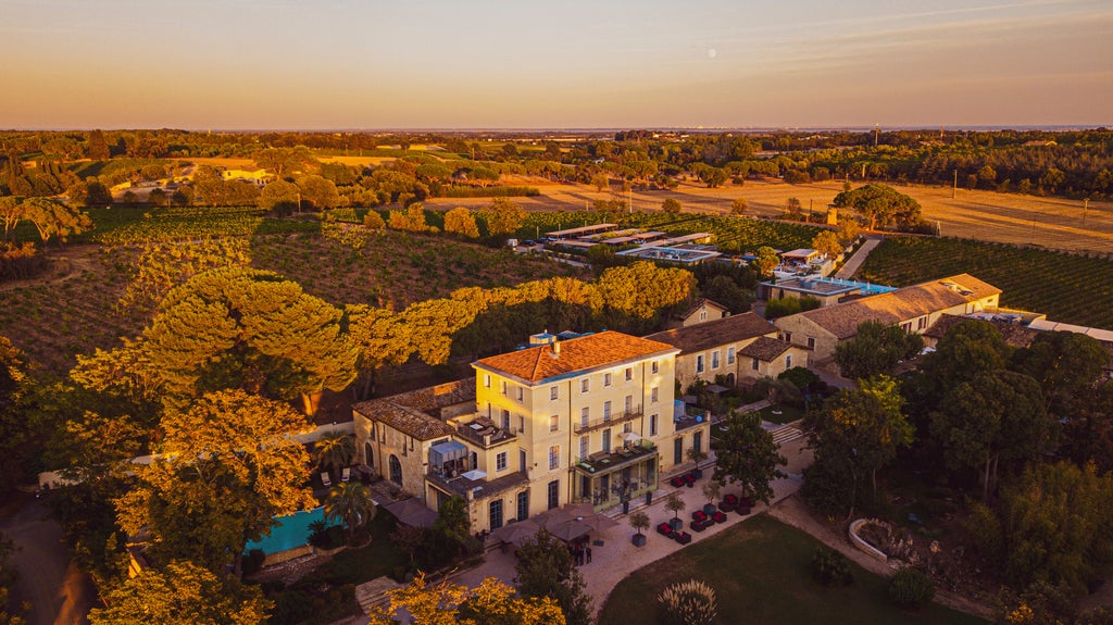 Elegant French chateau hotel with manicured gardens, stone facade, and arched windows surrounded by mature cypress trees at sunset