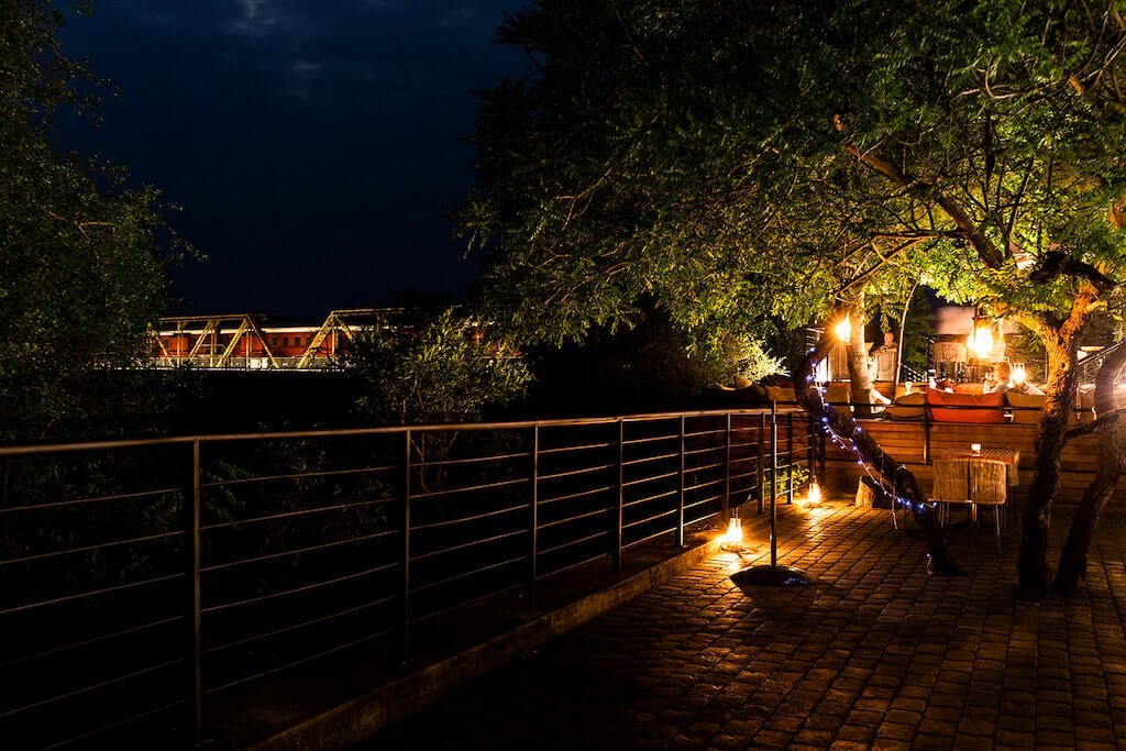 Historic train car converted into luxury hotel suite suspended above Sabie River in Kruger Park, featuring glass-walled rooms and deck