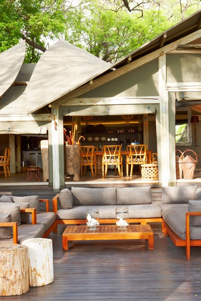 Elevated wooden walkway leading to luxurious safari tents nestled among palm trees, overlooking pristine Okavango Delta wetlands at sunset