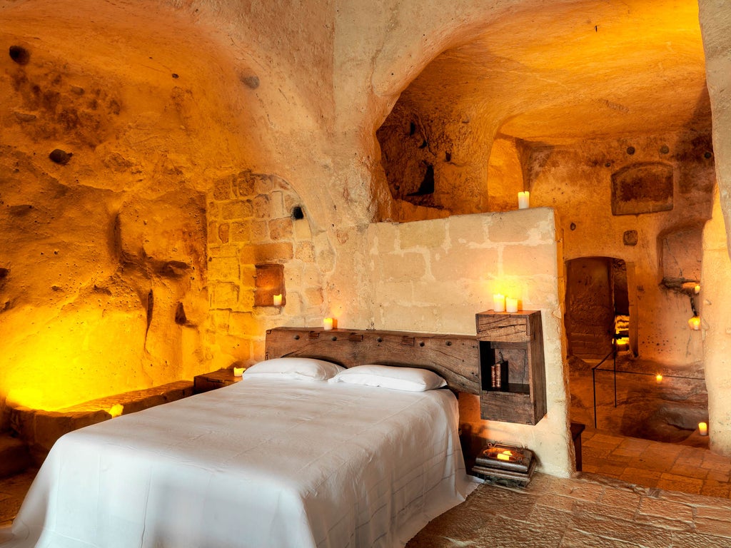 Cave hotel suite with rustic stone walls, dramatic archways, and romantic candlelit ambiance overlooking ancient Italian village