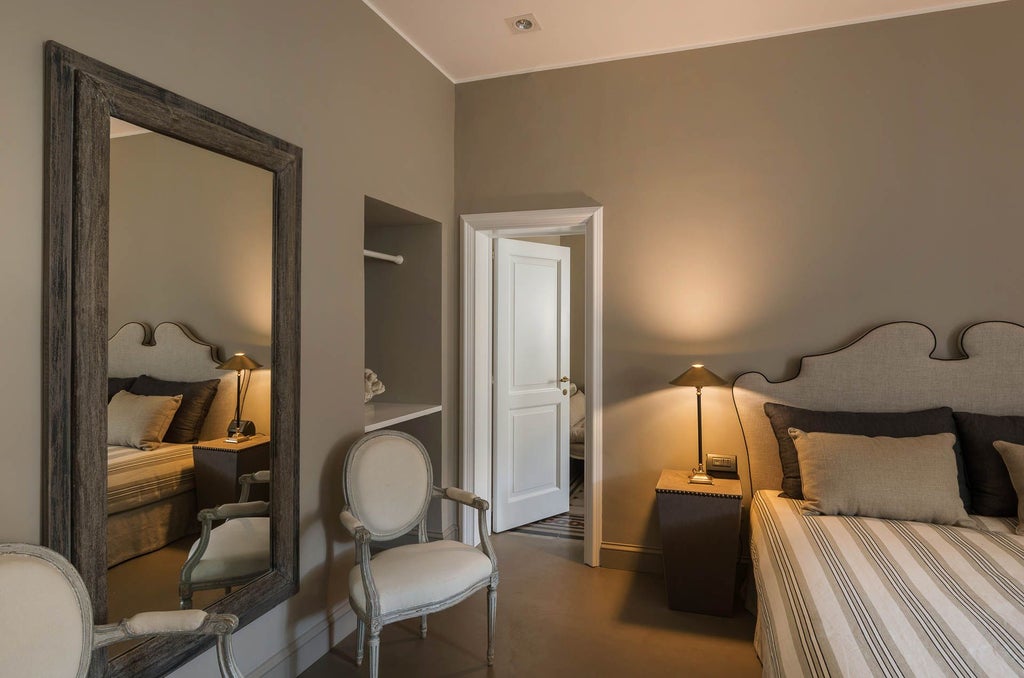 Elegant Italian deluxe studio with plush white bedding, arched window, antique wooden furniture, and soft natural light in Villadorata hotel room