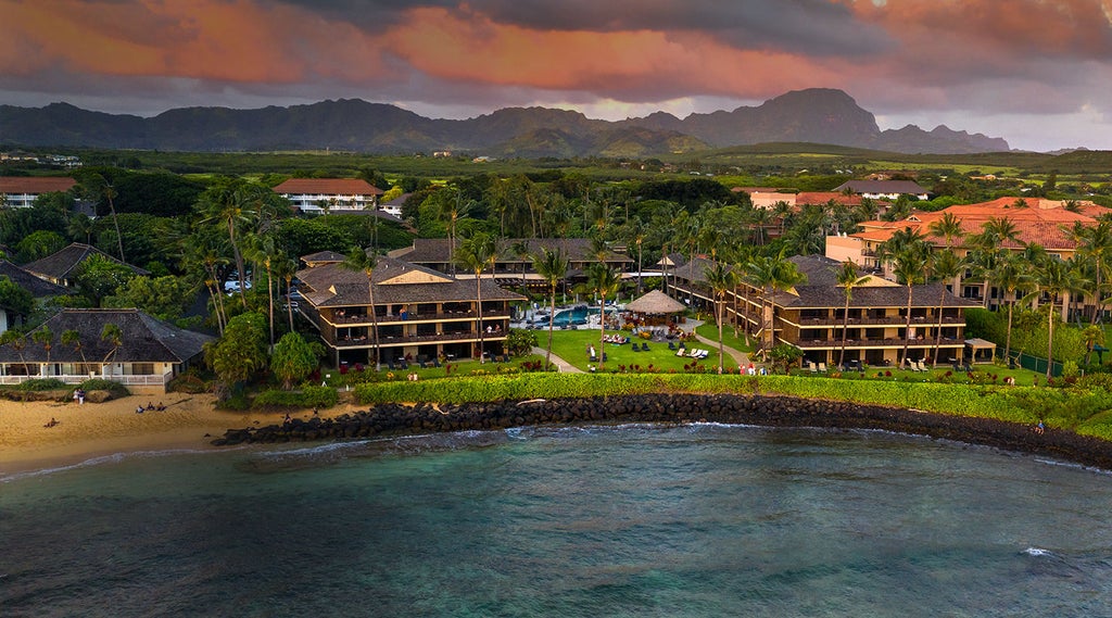 Beachfront luxury resort with infinity pool overlooking Pacific Ocean, palm trees and private cabanas under warm Hawaiian sunset