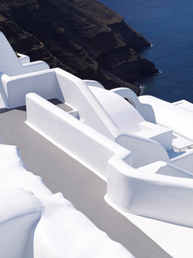 Luxurious white-washed Cycladic hotel with infinity pools cascading down terraced cliffs overlooking the azure Aegean Sea in Santorini, Greece