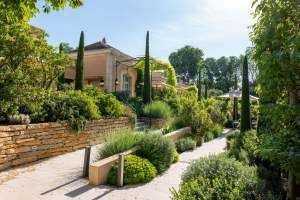 Elegant French villa with ornate white facade, manicured garden, wrought-iron balconies, and lush greenery against a soft blue sky in Provence