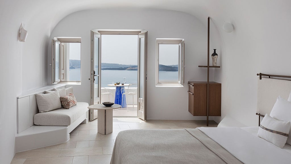 Elegant white Cycladic-style suite with minimalist design, private balcony overlooking azure Aegean Sea, featuring crisp linens and modern luxury in Oia, Santorini