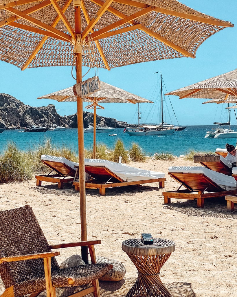 Pristine turquoise waters meet white sandy beaches along Ibiza's coastline, with luxury yachts anchored near cliff-side villas at sunset