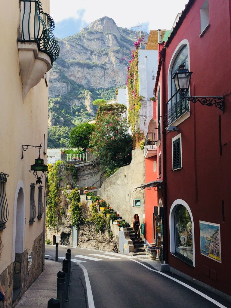 Luxurious wooden speedboat gliding along turquoise Mediterranean waters with Amalfi Coast's dramatic cliffs and colorful towns in background