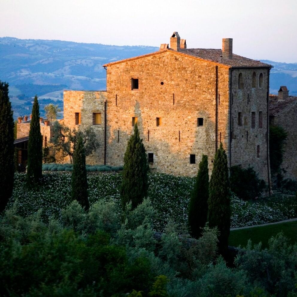 Rustic stone Tuscan castle with terracotta roof, nestled among rolling vineyards and olive groves at golden sunset, exuding timeless Italian countryside elegance