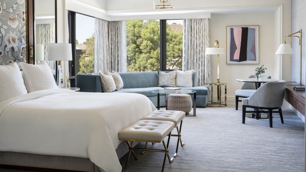 Spacious corner studio suite at Four Seasons Hotel with modern decor, plush king bed, elegant sitting area, and floor-to-ceiling windows overlooking scenic landscape