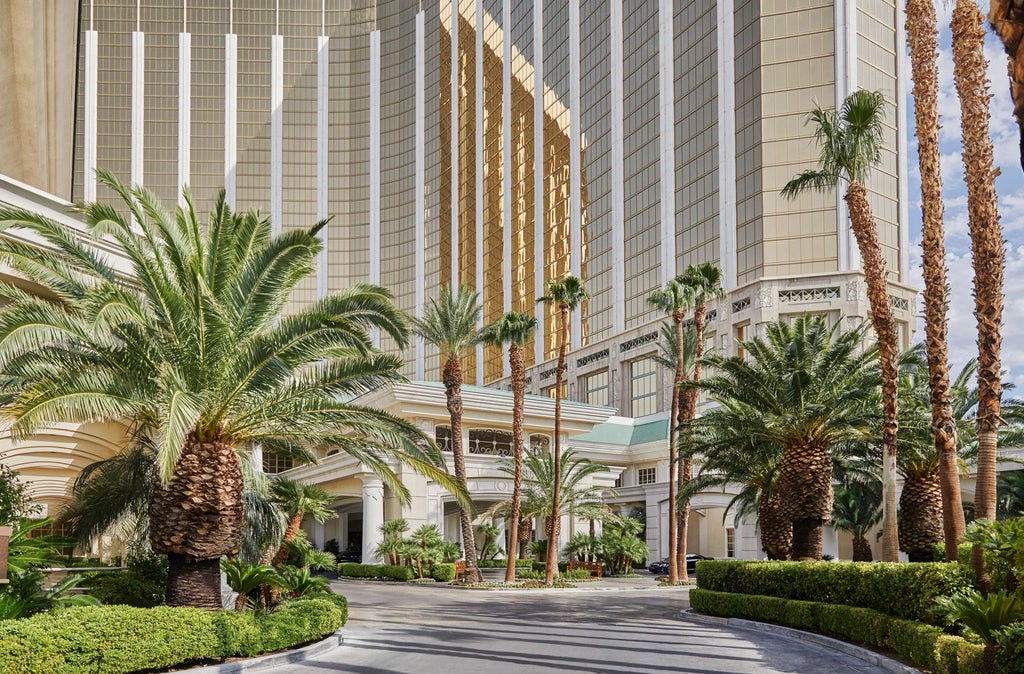 Luxurious Four Seasons Las Vegas hotel exterior with golden glass facade, palm-lined driveway, and dramatic desert mountain backdrop