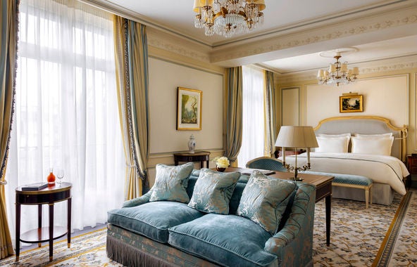 Opulent Ritz Paris suite featuring gilded Louis XV furniture, crystal chandelier, marble fireplace, and luxurious cream silk drapes and bedding