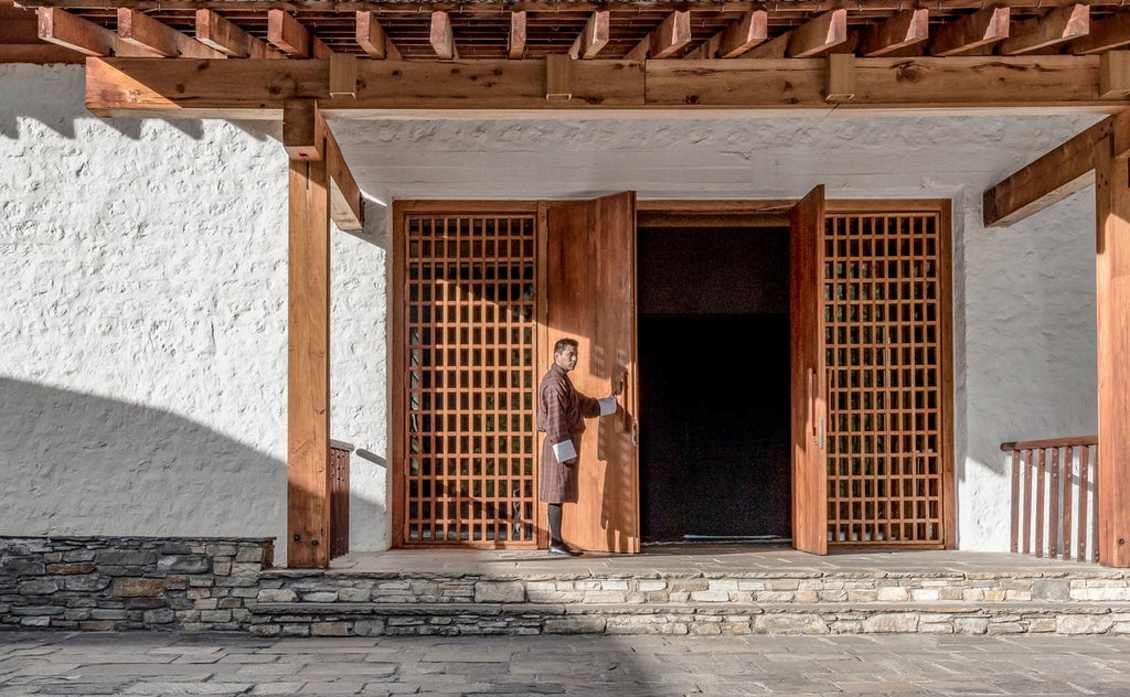 Traditional Bhutanese lodge with stone façade and ornate wooden details nestled in misty pine forest, featuring mountain views