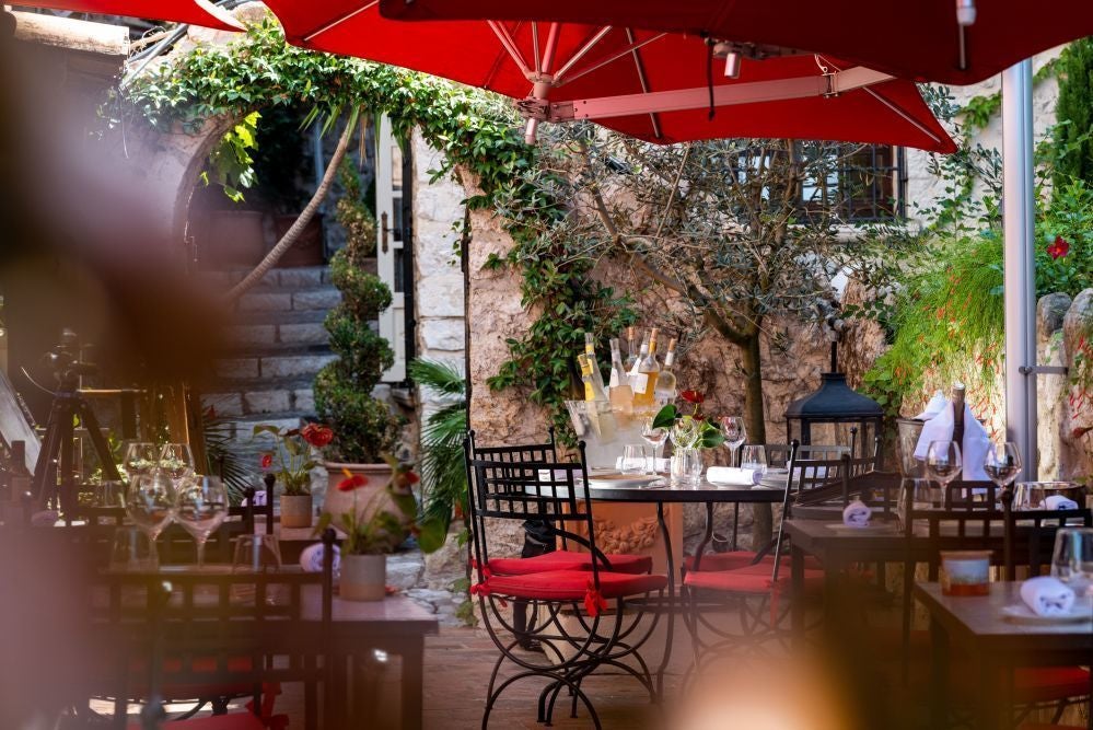 Elegant historic French hotel with stone facade, arched windows, and ivy-covered walls in charming Saint-Paul-de-Vence village surrounded by lush Mediterranean landscape