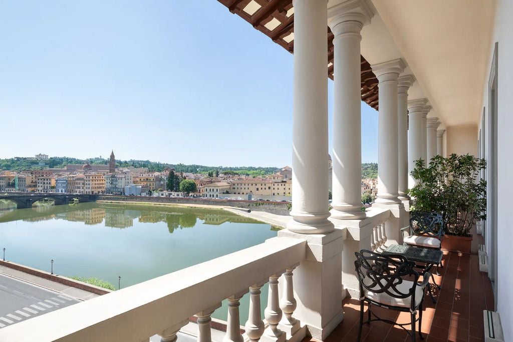 Historic St Regis Florence hotel exterior with ornate Renaissance architecture, golden lighting, and arched windows overlooking Arno River at dusk