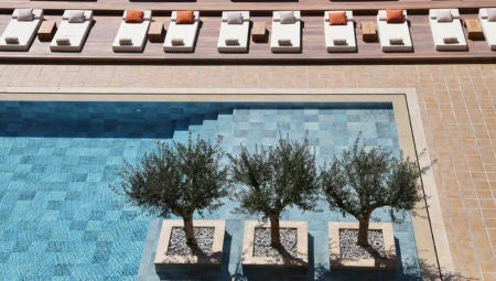 Elegant white Mediterranean hotel with palm trees, featuring a blue-lit infinity pool overlooking the sea at sunset in coastal Greece