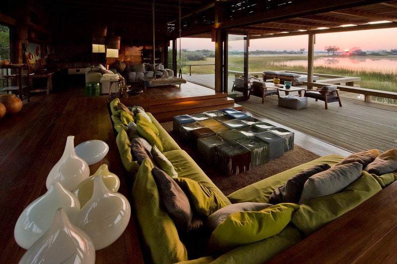 Elevated luxury safari lodge overlooking grasslands, featuring thatched-roof suites with private decks and plunge pools at sunset