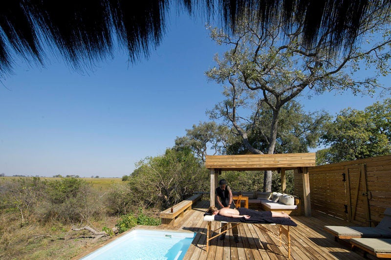 Elevated wooden luxury safari lodge with modern design overlooking vast Okavango grasslands during golden sunset hour