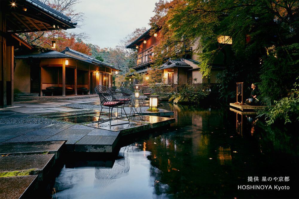 Traditional Japanese ryokan with wooden architecture set against misty mountains, featuring serene water gardens and lantern-lit pathways