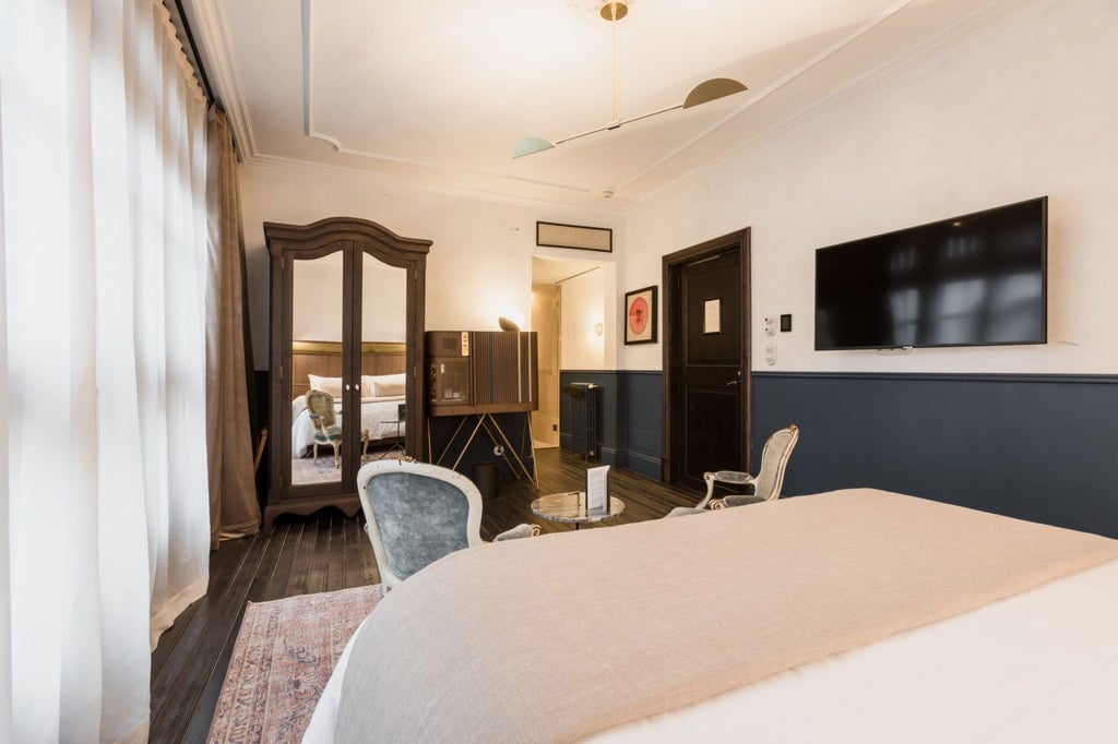 Elegant junior suite with plush white bedding, antique wooden furniture, and soft natural light in historic Spanish luxury hotel room