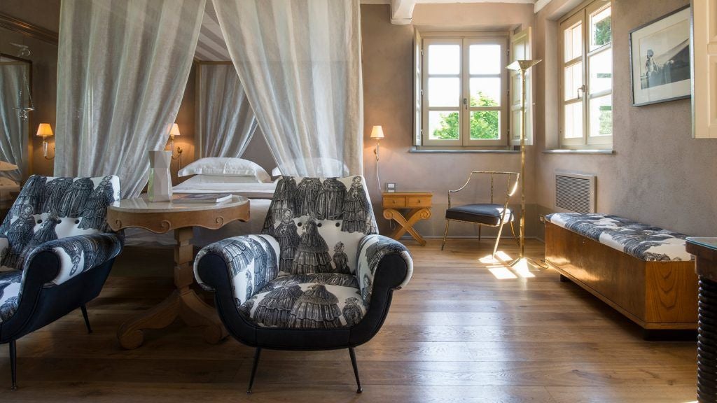 Elegant Italian boutique hotel room with minimalist white decor, wooden floors, and panoramic Tuscan countryside view through large windows