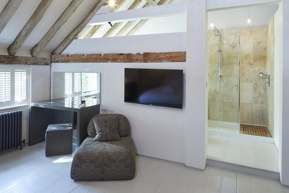 Luxurious rustic hotel room at Tuddenham Mill, featuring exposed wooden beams, crisp white linens, and contemporary minimalist design with natural light.