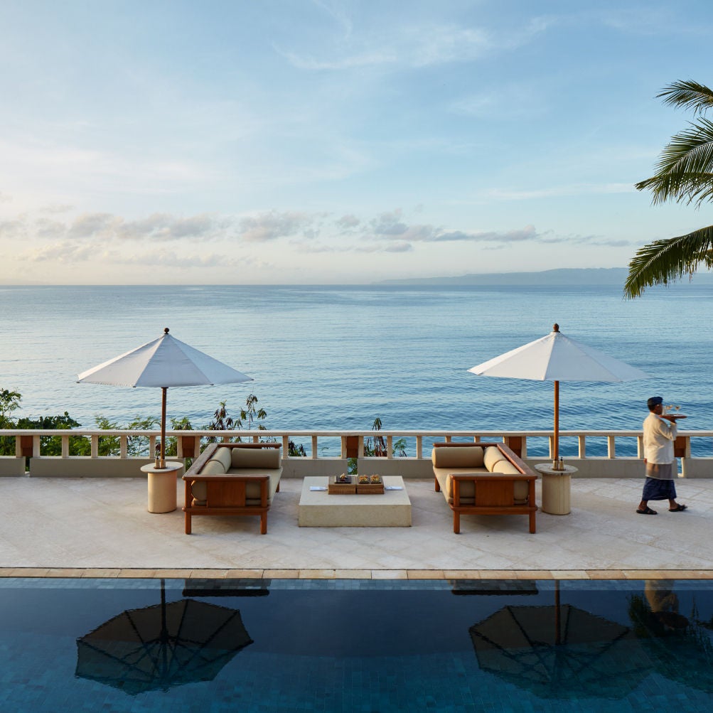 Three-tiered infinity pools cascading down a hillside with Bali Sea views, surrounded by tropical gardens and private luxury suites