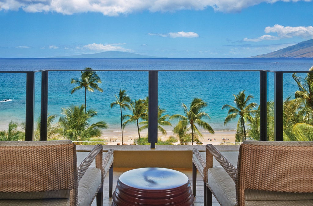 Oceanfront luxury resort with infinity pools overlooking Maui coastline, featuring palm trees and white umbrellas at sunset