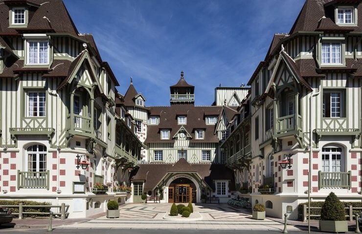 Elegant white and black timber-framed facade of Le Normandy Hotel in Deauville, featuring ornate Belle Époque architecture and manicured gardens