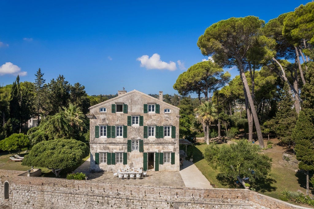 Stone villa with white walls and terracotta roof overlooking azure Aegean Sea, featuring elegant Mediterranean gardens and a sun-drenched outdoor terrace with traditional Greek architectural elements