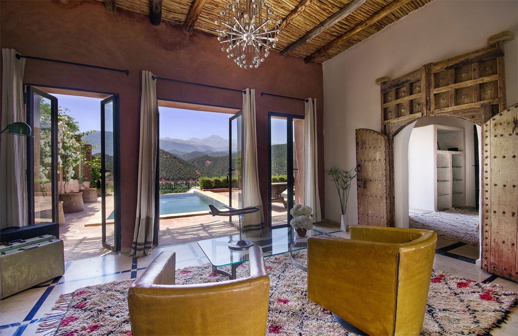 Luxurious terracotta Moroccan hotel perched on hilltop overlooking Atlas Mountains, with traditional architecture and lush gardens