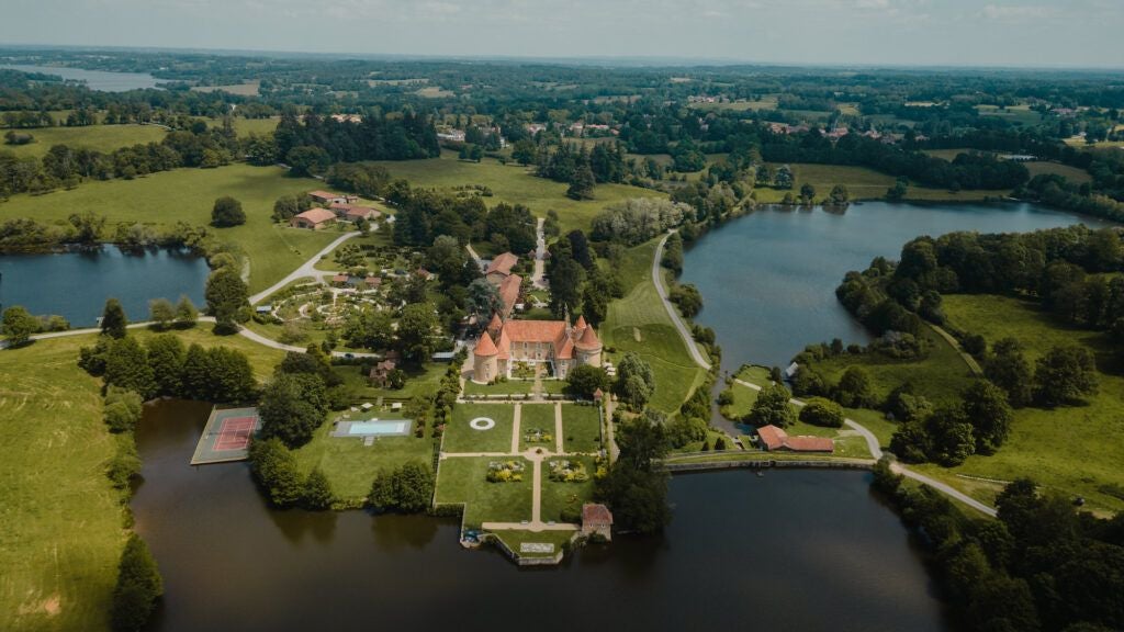 Luxurious French château-style hotel nestled in verdant countryside, featuring stone architecture, expansive green lawns, and elegant architectural details