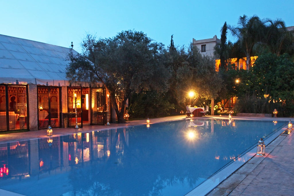 Ornate Moroccan riad courtyard with intricate archways, candlelit lanterns, and emerald pool surrounded by traditional cushioned seating