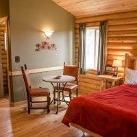 Rustic wooden cabin interior with plush king bed, mountain view windows, and warm earth-toned decor at scenset Mountain Ranch Preserve accommodation