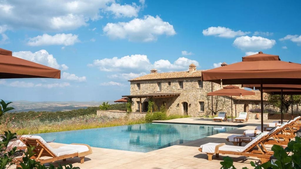 Luxurious Tuscan villa resort with stone facade, cypress trees and manicured gardens overlooking rolling Italian countryside at sunset