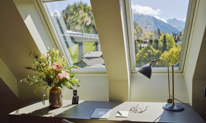 Elegant Swiss alpine hotel suite with panoramic mountain view, plush king bed, crystal chandelier, and modern marble bathroom in soft neutral tones