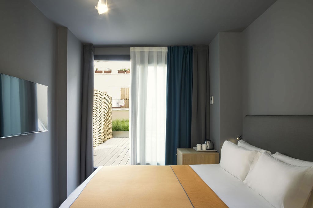 Elegant hotel room with private terrace overlooking Barcelona, featuring modern white bedding, wood floors and sleek glass doors