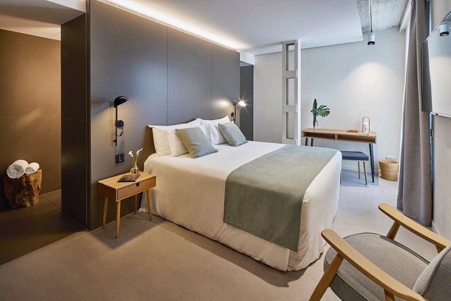 Minimalist modern hotel room with white walls, sleek wooden furniture, large window, elegant design highlighting contemporary Spanish hospitality aesthetic