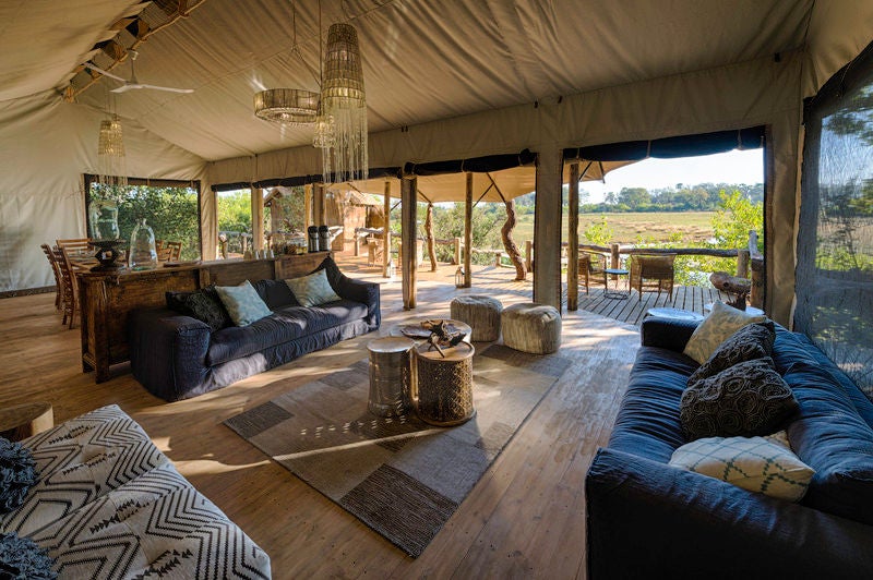 Elevated luxury safari tent with private deck overlooking lush African savanna, nestled among trees at golden hour