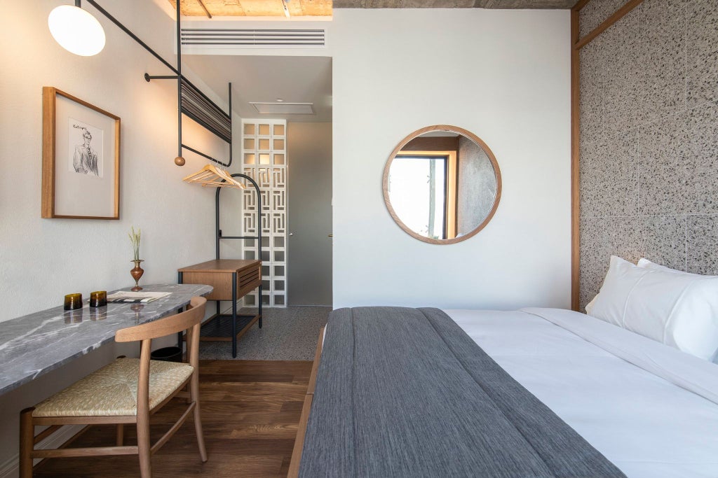 Minimalist Greek hotel room with warm wood accents, crisp white linens, and large windows overlooking urban Athens landscape at golden hour