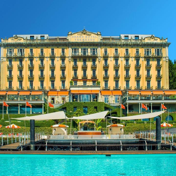 Elegant lakeside hotel with Art Nouveau facade, grand terraces, and vibrant gardens overlooking Lake Como's blue waters at sunset