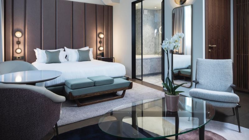 Elegant junior suite with soft neutral tones, modern design elements, plush king bed, and sophisticated Parisian-style decor in a chic boutique hotel room