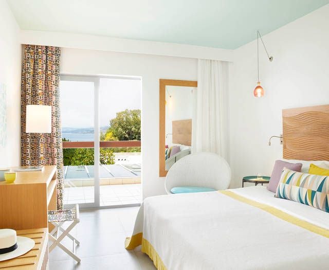 Elegant double room at Eagles Palace hotel with expansive Aegean Sea views, crisp white linens, modern wooden furnishings, and panoramic blue horizon backdrop