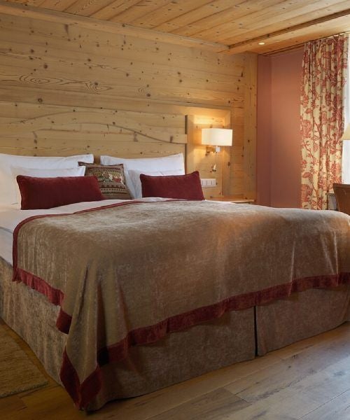 Elegant chalet-style hotel room with wooden panels, plush armchairs, private balcony, and mountain views in upscale Swiss resort